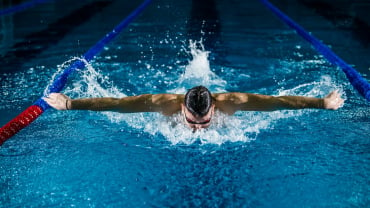 Man doing butterfly stroke in an indoor swimming pool.