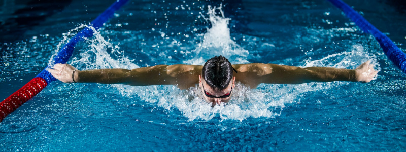 Man doing butterfly stroke in an indoor swimming pool.