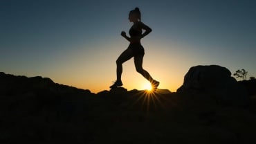 Silhouette of a person running along a rocky landscape.