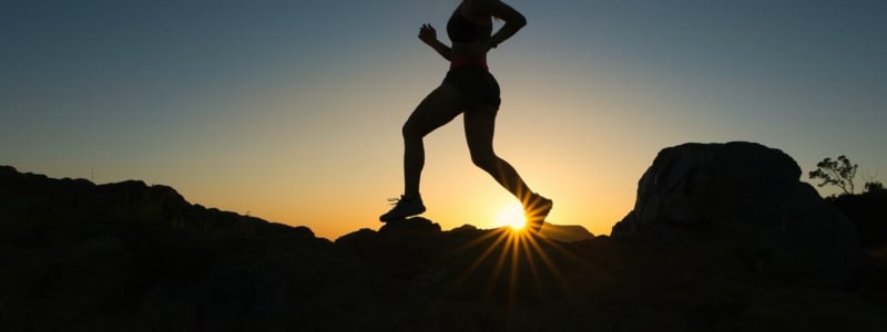 Silhouette of a person running along a rocky landscape.