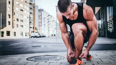 Man in running gear crouching down to tie his trainer laces