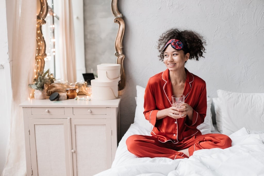 Woman sitting on a bed in red pyjamas wearing an eye mask on her forehead