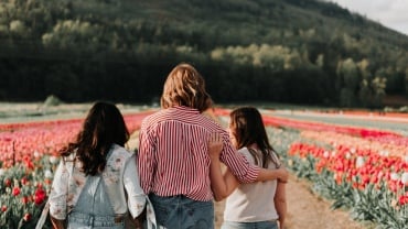 A woman and two older children walking in a field of red flowers