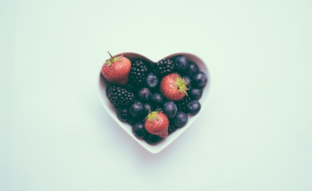 Blueberries, strawberries and blackberries in a white heart-shaped bowl.