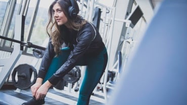 Woman wearing headphones in a gym doing up her trainers, which are gym bag essentials