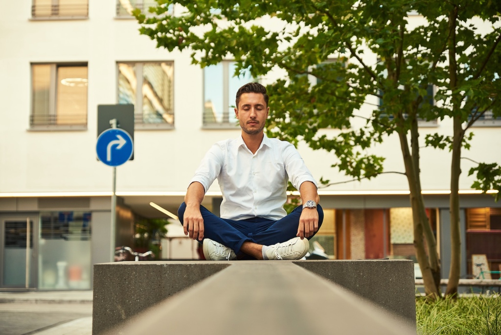 A man meditating on a raised concrete block on a city street.