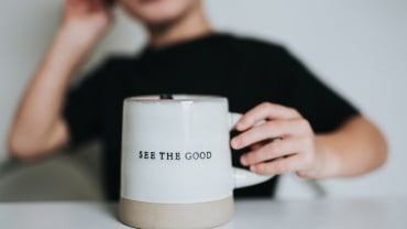 Person in a black top holding a white mug that says 'see the good'