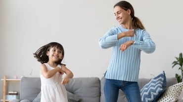 An adult woman dancing in a living room with a child