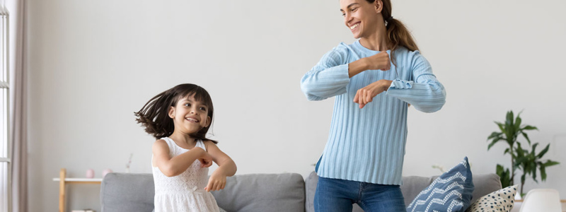 An adult woman dancing in a living room with a child