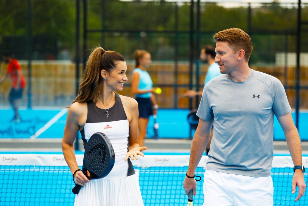 A man and a woman on a Padel court smiling at each other.