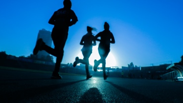 Three people running silhouetted against a blue sky