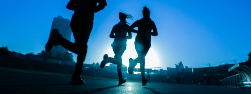 Three people running silhouetted against a blue sky