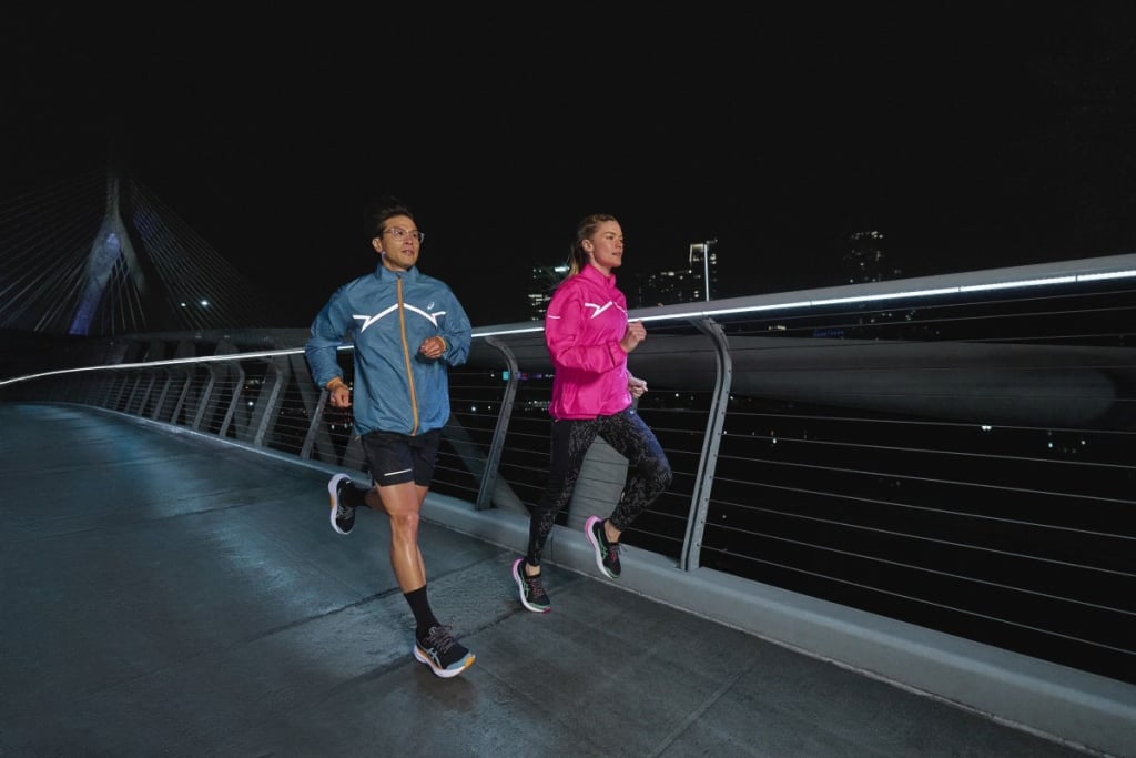 Two runners running across a bridge at night in a city.