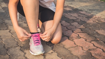 A person crouched down on pavement tying up a running trainer on their foot