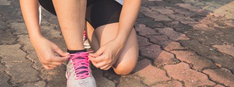 A person crouched down on pavement tying up a running trainer on their foot