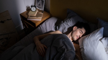 Man sleeping peacefully in bed as sunlight streams over his face and pillows