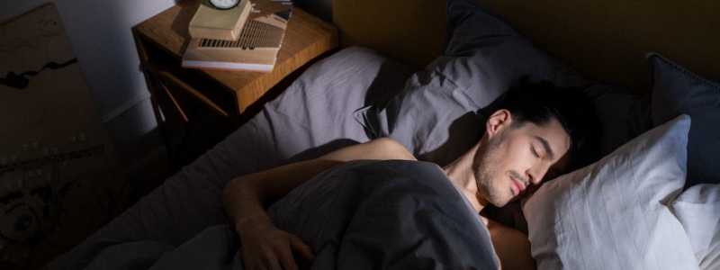 Man sleeping peacefully in bed as sunlight streams over his face and pillows