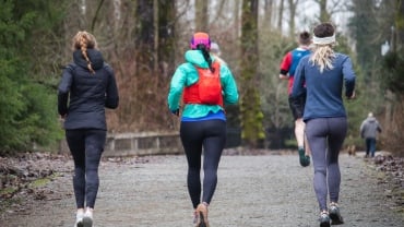 Three women running outdoors, shot from behind, against a grey sky