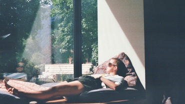 Person lying on a window seat looking out of the window as the sun streams in.