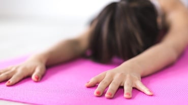 Woman stretching forwards on a yoga mat, her head bent towards the floor