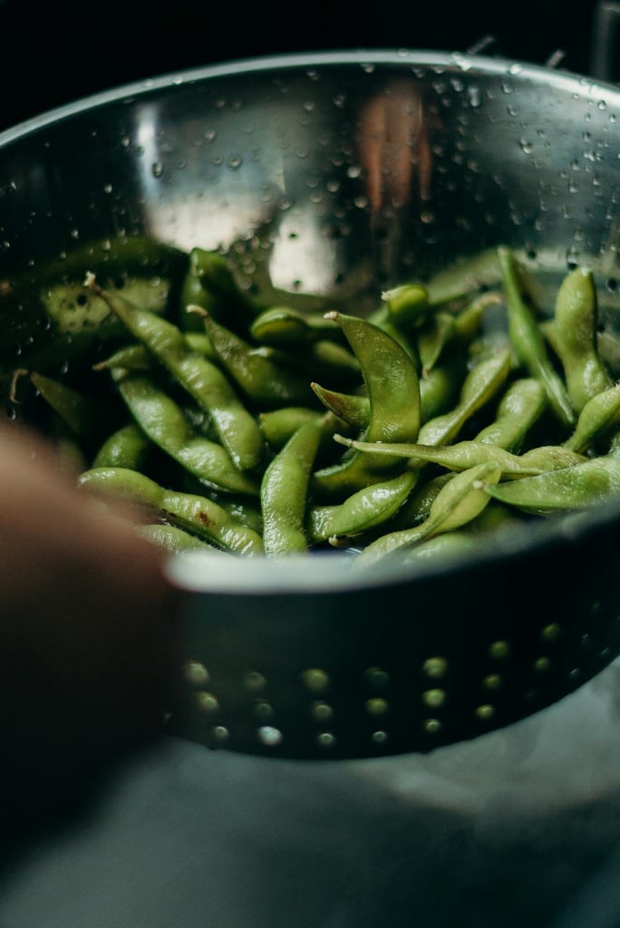 Green edamame pods in a colander.