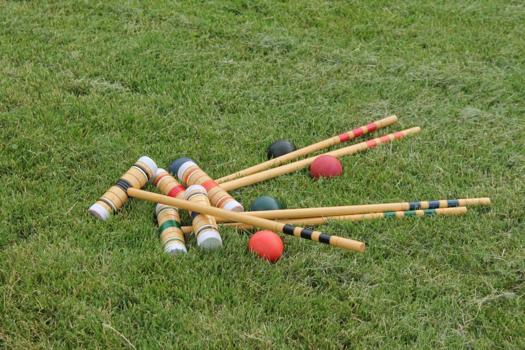 Colourful croquet mallets and balls lying on green grass.