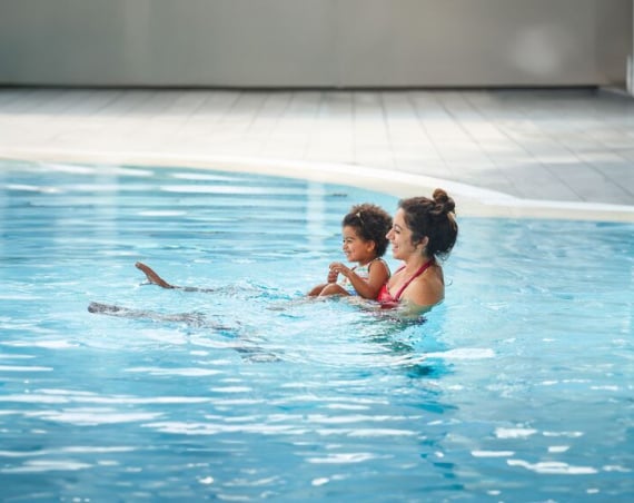 A woman and a girl in an outdoor swimming pool, both smiling.