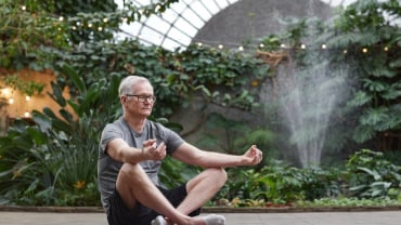 Man sitting cross-legged, eyes closed, hands in a yoga mudra - he appears to be meditating.