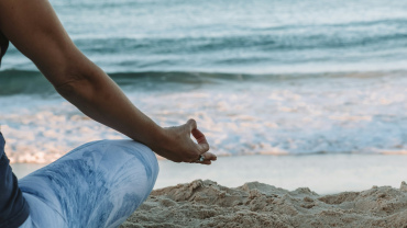 Close up of a person on a beach in a meditation pose.