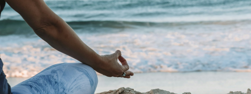 Close up of a person on a beach in a meditation pose.