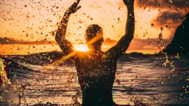 Silhouette of a person splashing in an outdoor body of water against the sunset.