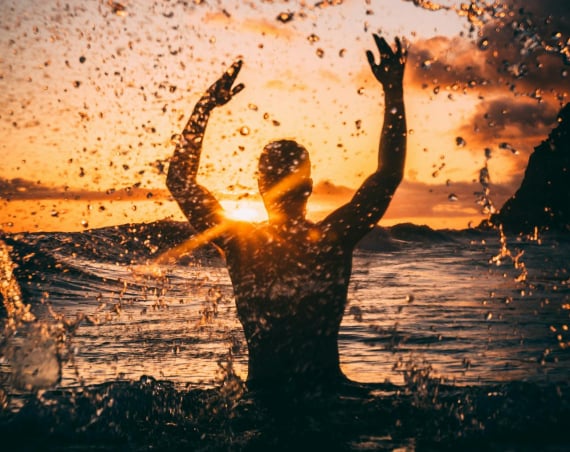 Silhouette of a person splashing in an outdoor body of water against the sunset.