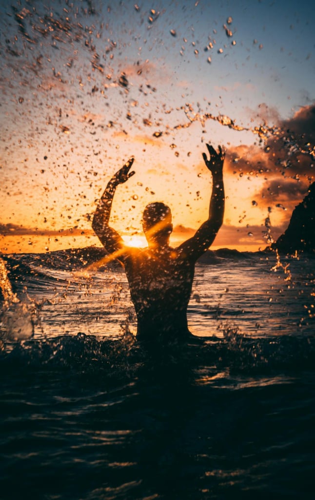 Silhouette of a person splashing in an outdoor body of water against the sunset.