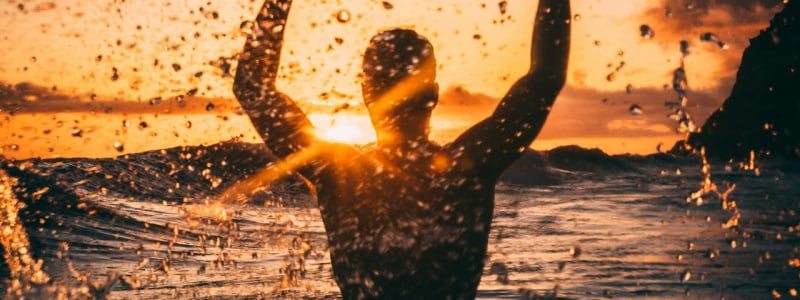 Silhouette of a person splashing in an outdoor body of water against the sunset.