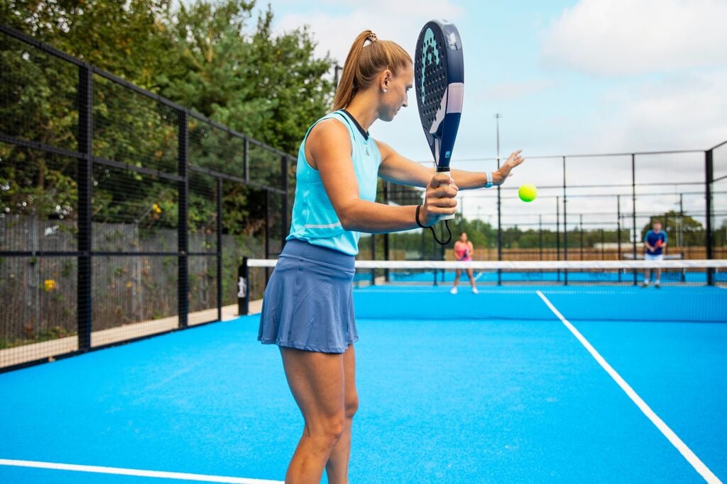 A woman on a Padel court about to serve the ball.