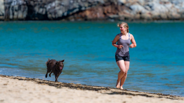 Woman running along a beach with a dog.