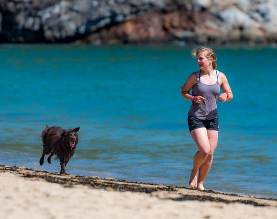 Woman running along a beach with a dog.