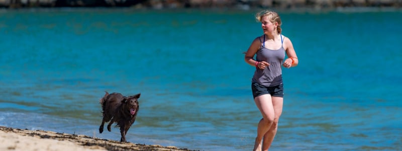 Woman running along a beach with a dog.