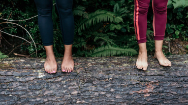 Two women standing barefoot on a log.