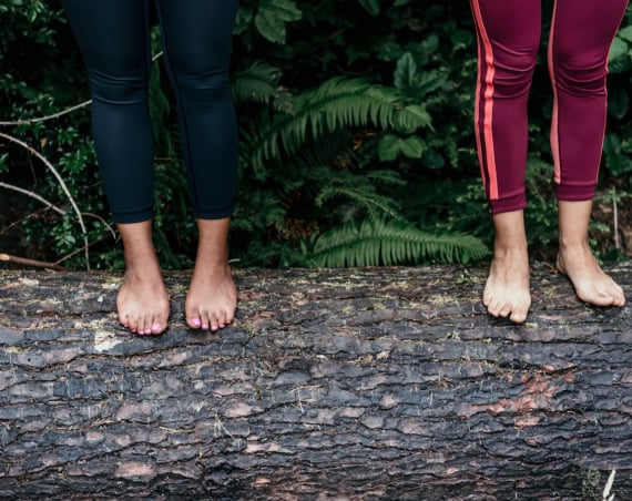 Two women standing barefoot on a log.