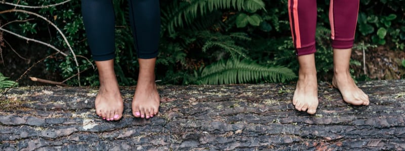 Two women standing barefoot on a log.