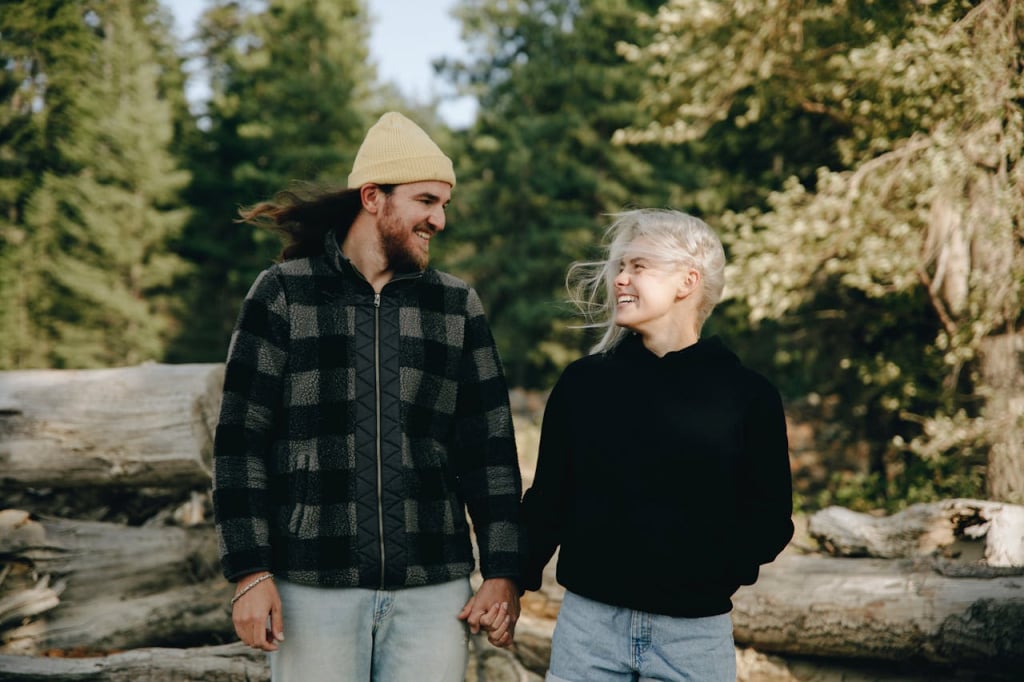 A couple smiling at each other in front of a forest.