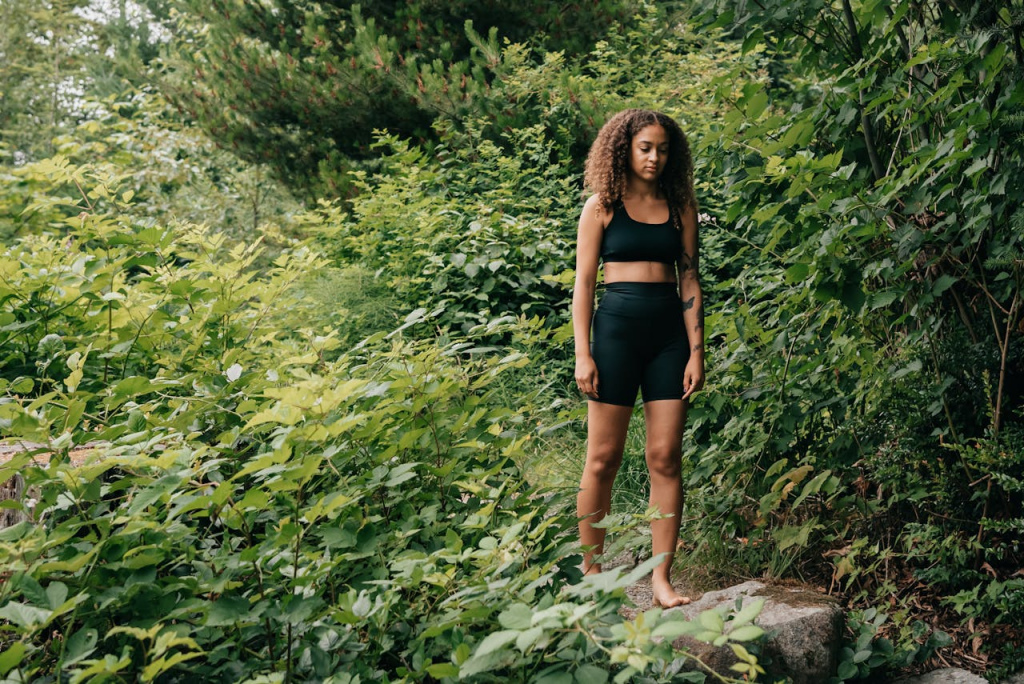 A woman standing with her eyes closed outdoors, surrounded by greenery.