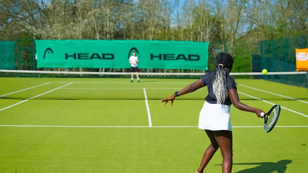 A woman and a man playing tennis on an outdoor court at a David Lloyd club.