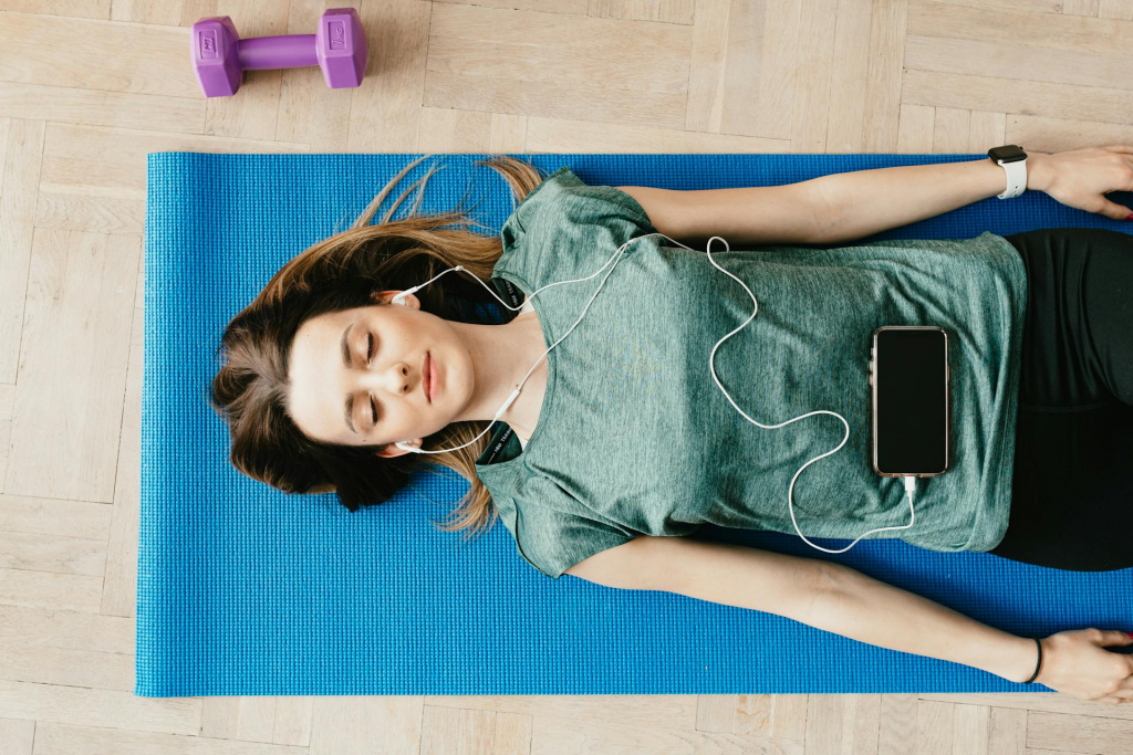 Woman lying on a yoga mat wearing headphones that are plugged into a phone.