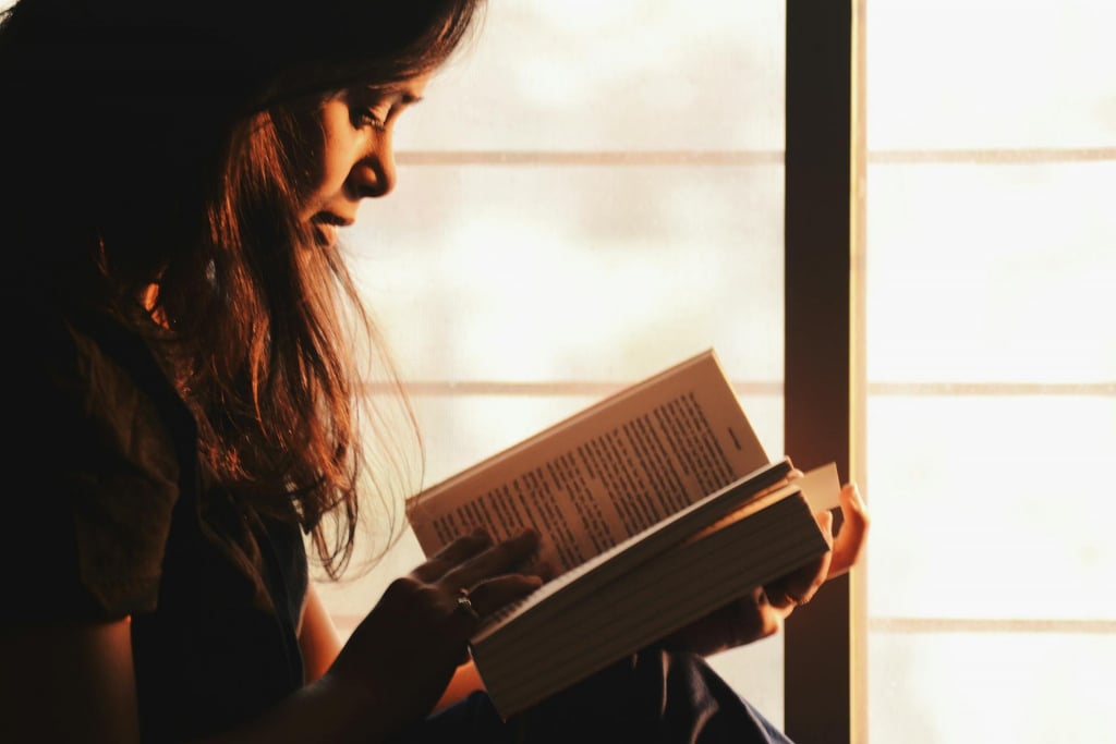 A woman reading a book by a window.