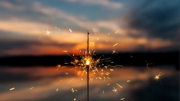 A lit sparkler held up against a sunset.