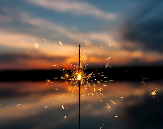 A lit sparkler held up against a sunset.