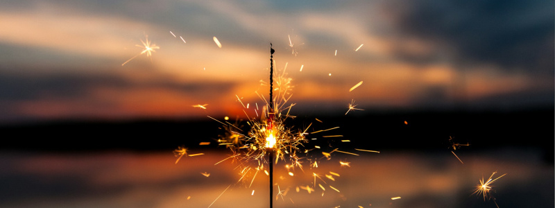 A lit sparkler held up against a sunset.