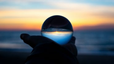 A hand holding a glass ball that's reflecting the sea; there's a sense it's some kind of crystal ball.